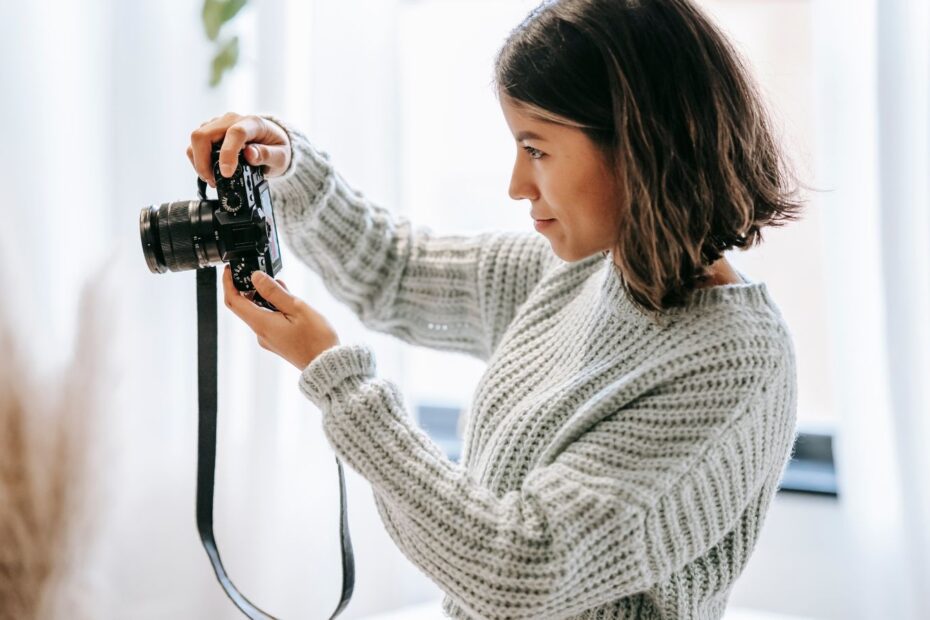 Female photographer in a grey sweater shooting a picture of a bathroom on a camera.